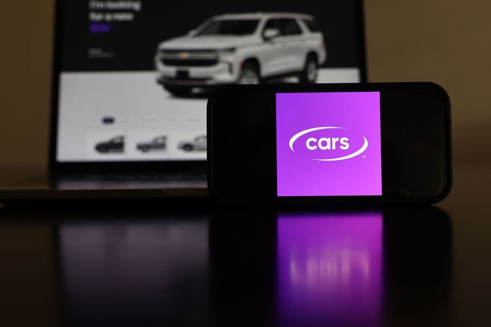 In this photo illustration, the Cars.com logo and web page are displayed on a cell phone and computer monitor on May 9, 2024 in Los Angeles, California.