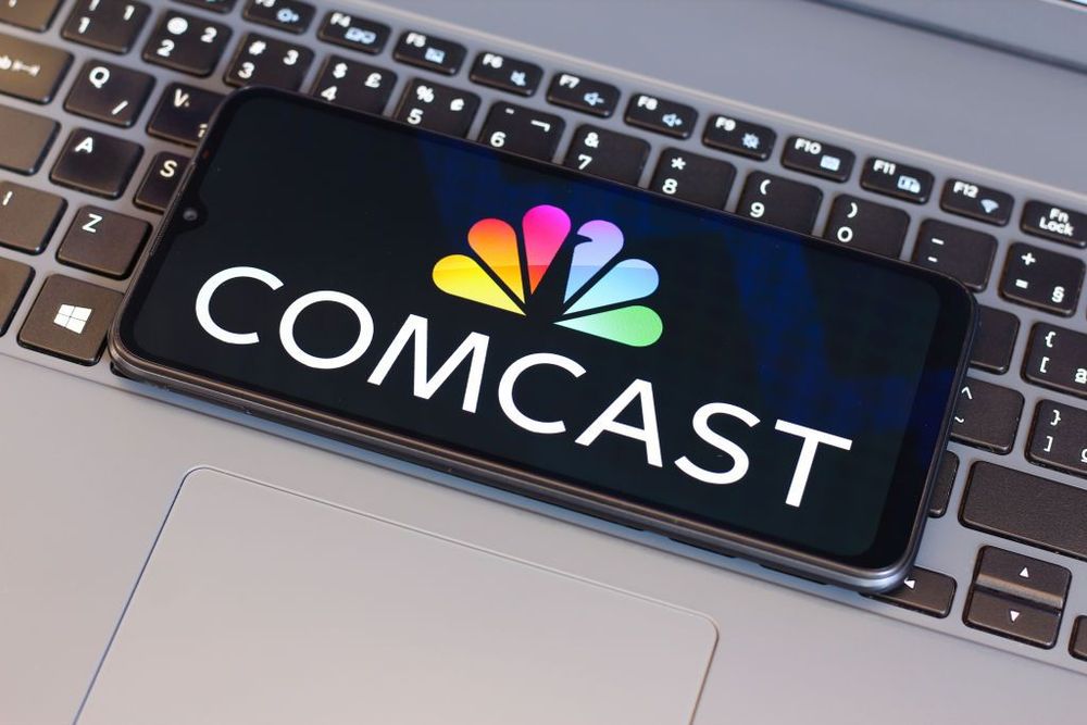  In this photo illustration, the Comcast Corporation logo is seen displayed on a smartphone screen next to a laptop keyboard.
