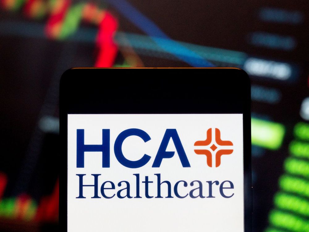 In this photo illustration, HCA Healthcare’s logo is on a smartphone with an economic stock exchange index graph in the background. (Photo Illustration by Budrul Chukrut/SOPA Images/LightRocket via Getty Images) 