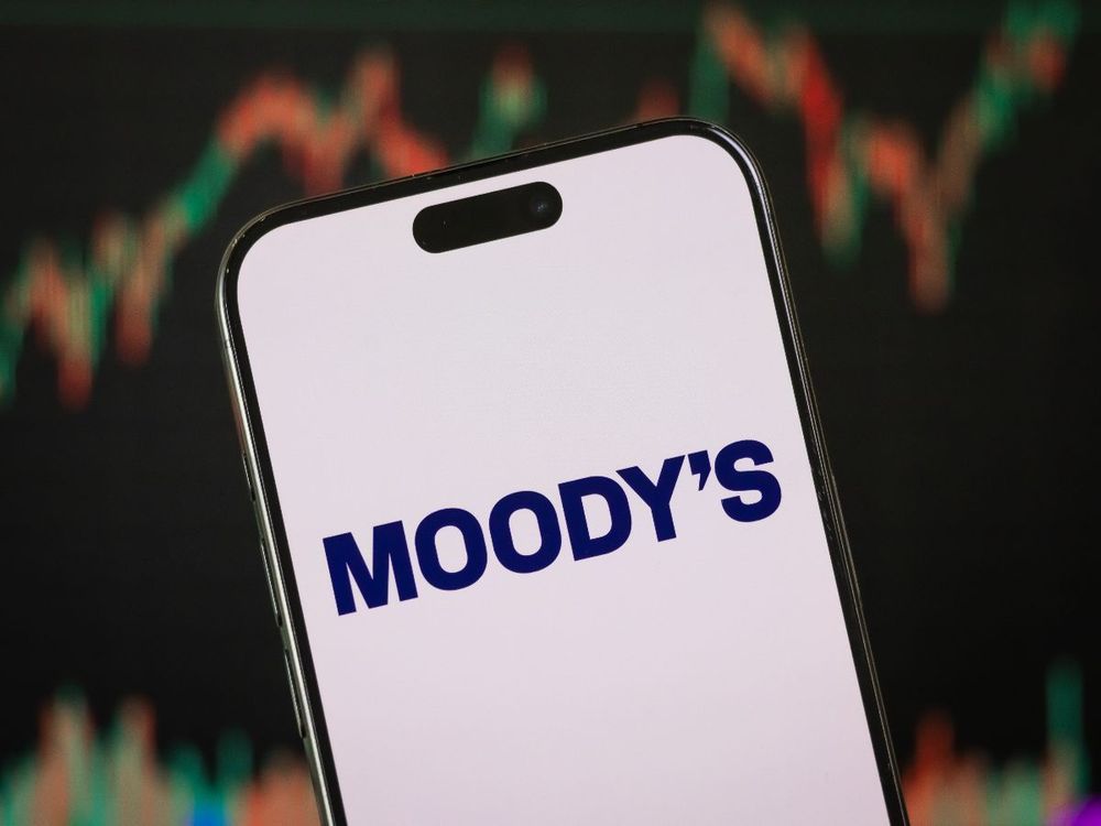In this photo illustration, the Moody's logo is displayed on a smartphone screen in front of a stock chart showcasing Moody's financial performance on Feb. 10, 2025, in China. (Photo illustration by Cheng Xin/Getty Images)
