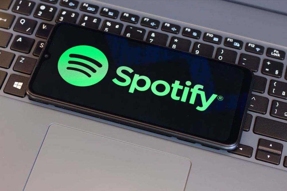 In this photo illustration, the Spotify logo is seen displayed on a smartphone screen next to a laptop keyboard.