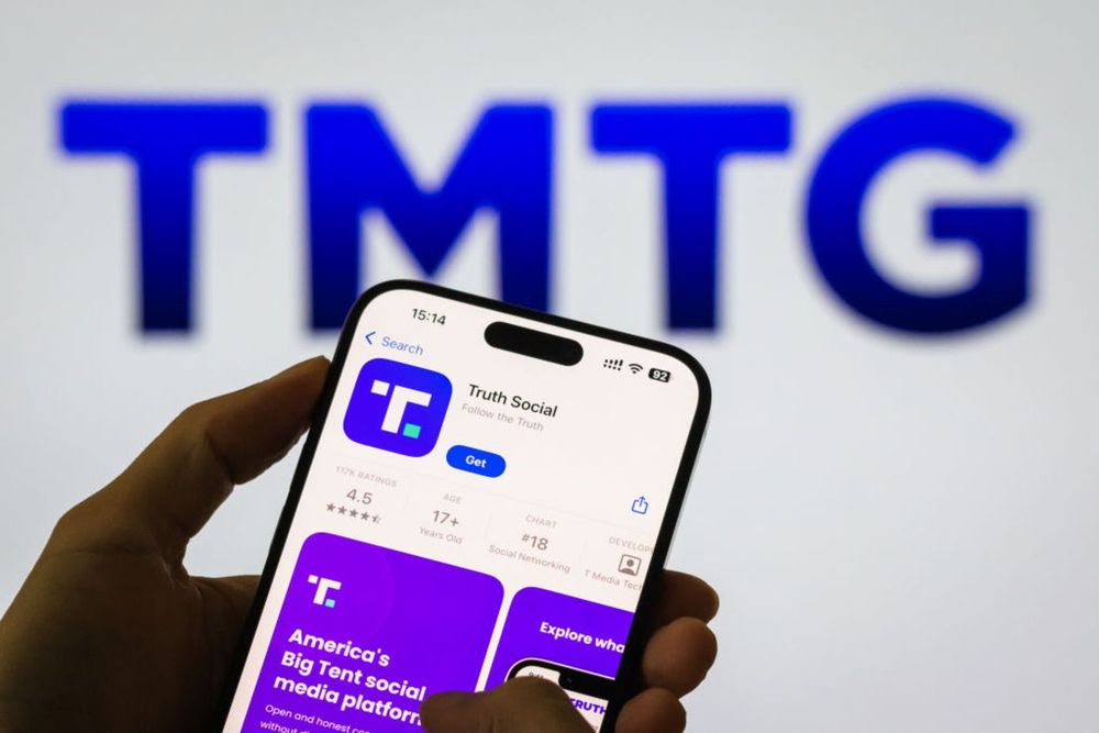 A person holds a smartphone displaying the Truth Social app page on the Apple App Store, with the Trump Media & Technology Group logo visible in the background, on November 6, 2024, in Chongqing, China.